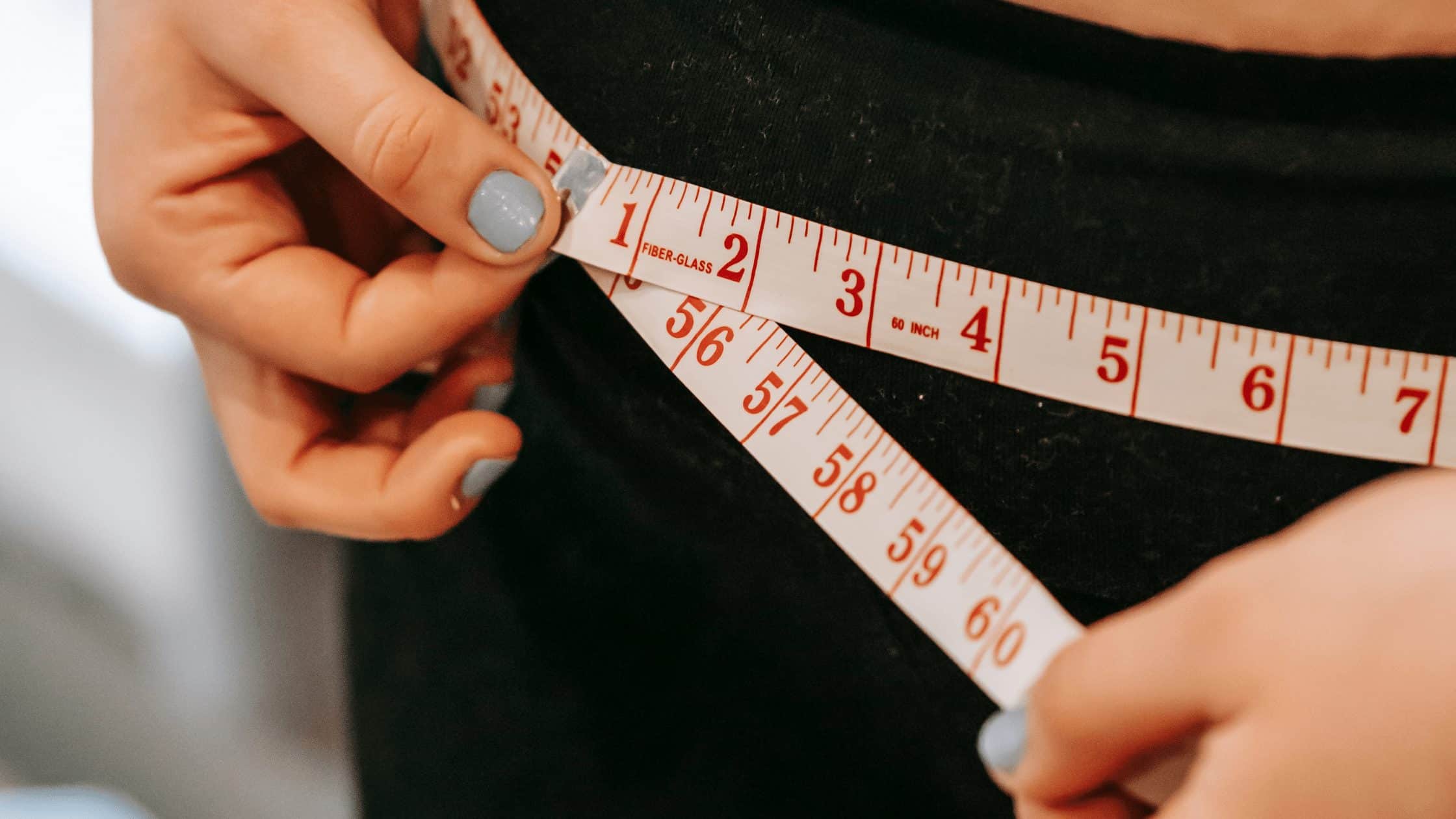 female measuring her waistline with measuring tape